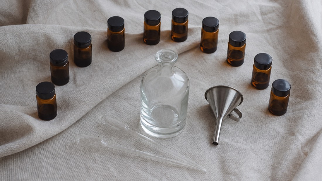 Flat lay of a blank 50 ml perfume bottle, glass pipettes and small amber vials arranged on natural linen