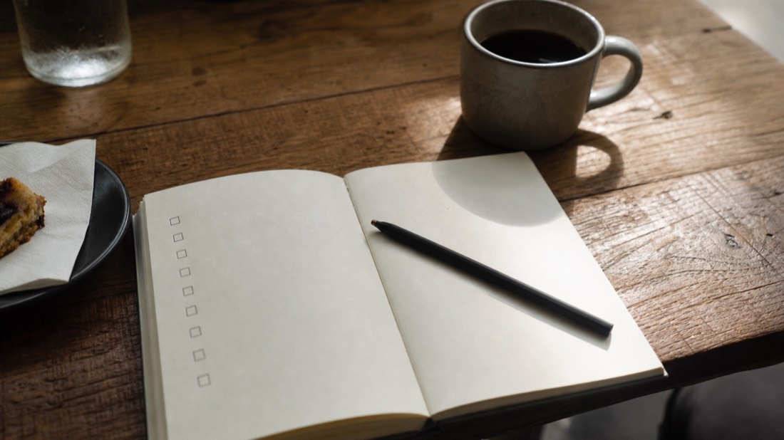 Open notebook with a pen and empty tick boxes beside a coffee, working through a tour booking checklist