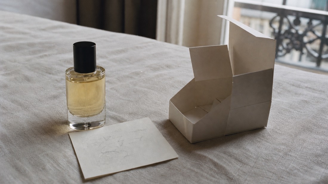 Perfume workshop gift set on linen: filled glass bottle, formula card and packaging box arranged in soft daylight