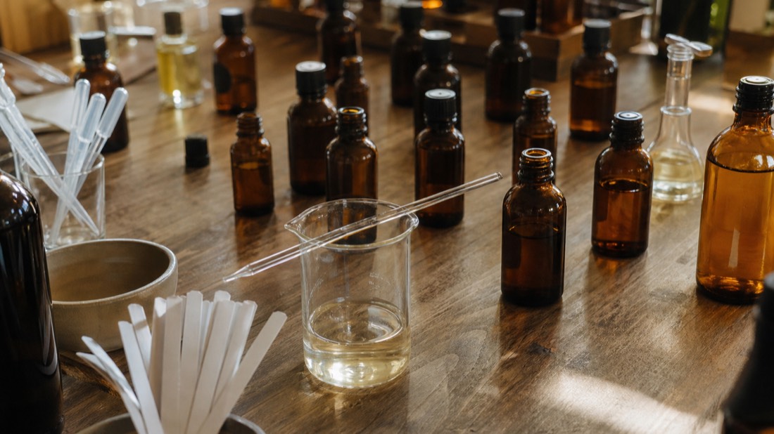 Glass beaker, pipette and small amber vials arranged for blending on a wooden perfume workshop bench