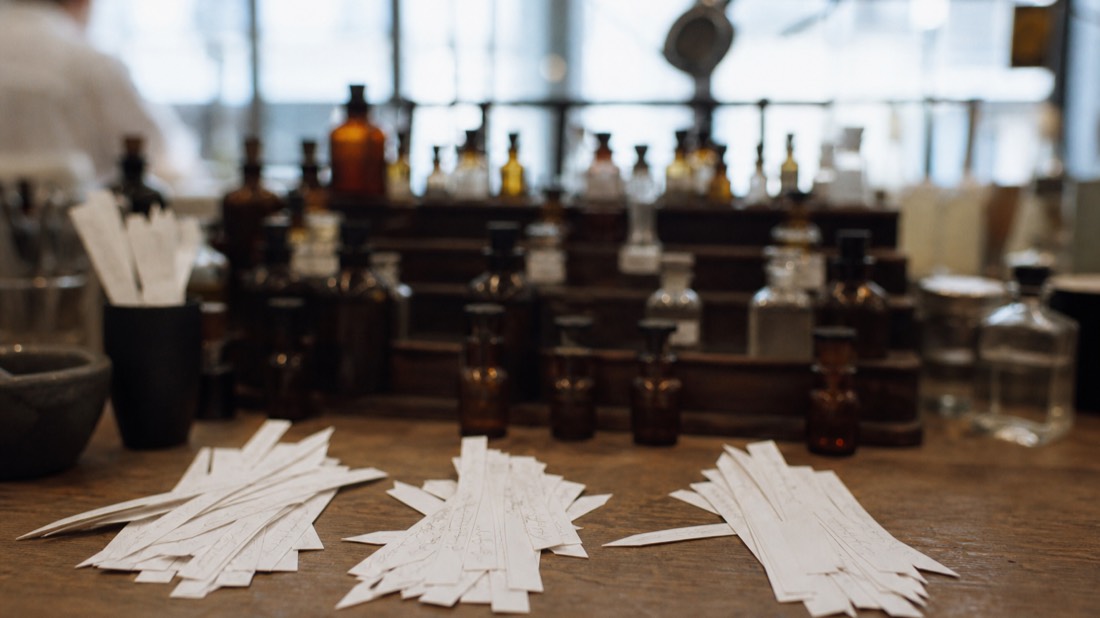 Fanned labeled scent strips sorted into piles beside tiered amber essence bottles at a Paris perfume workshop