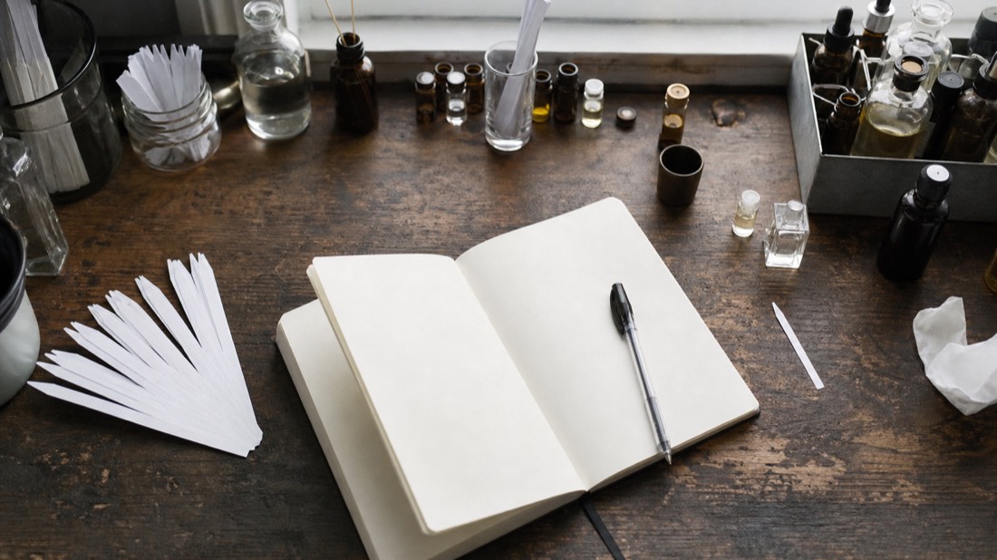 Notebook, scent strips and small vials laid out on a Paris workshop bench for planning a fragrance