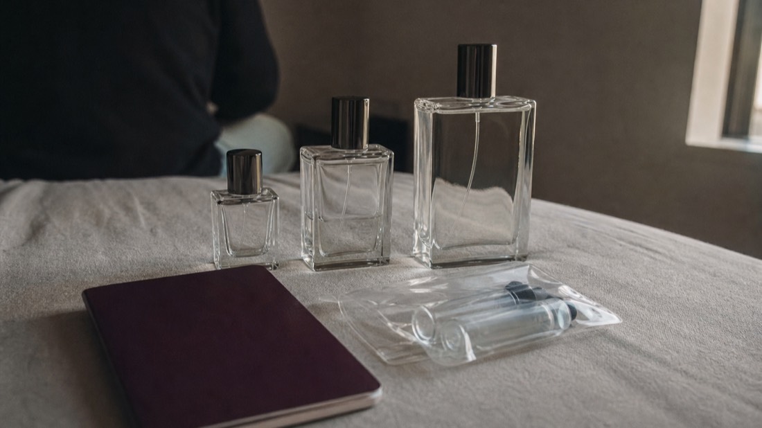 Three unlabeled perfume bottles of increasing size lined up on pale linen beside a passport and folded liquids bag