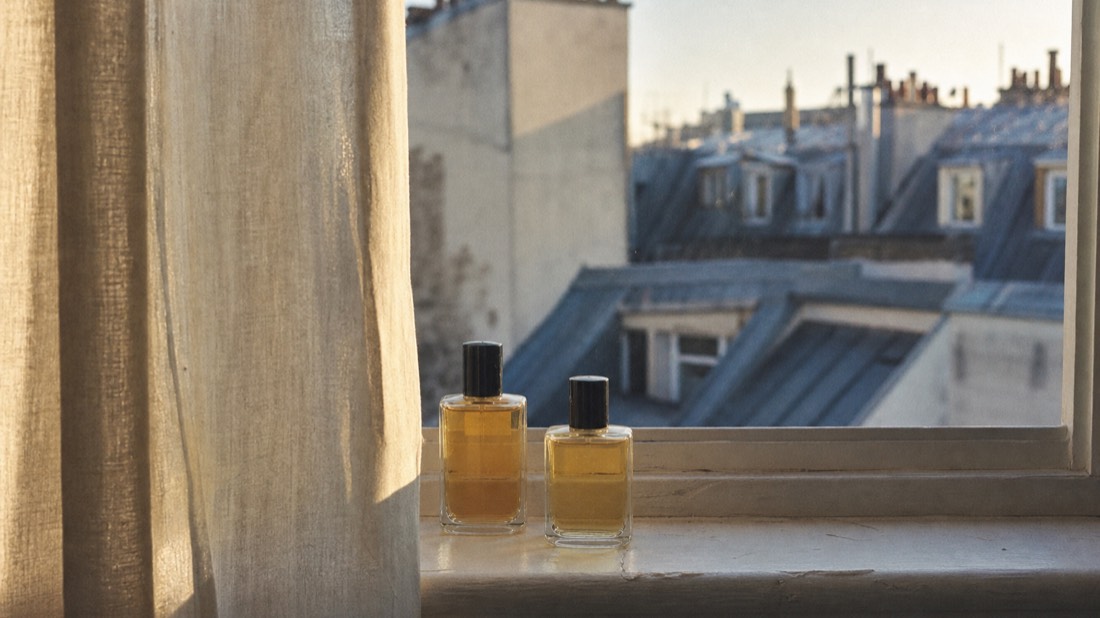 Two finished workshop perfume bottles side by side on a windowsill overlooking Paris rooftops, a couple's verdict