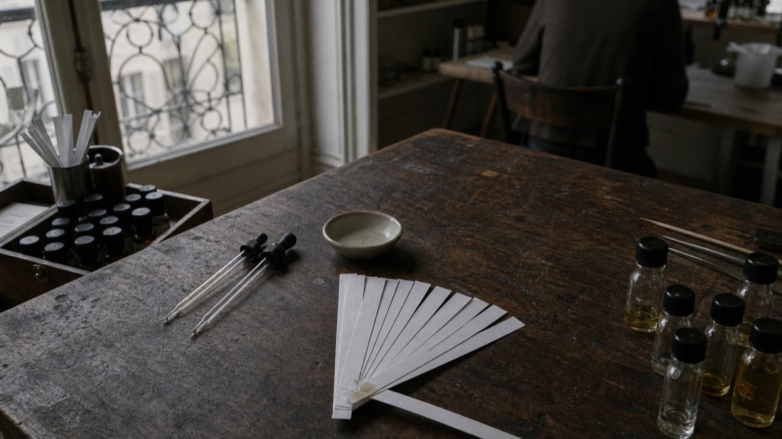Fanned paper scent strips and glass pipettes on a workshop table in Paris, learning perfume structure hands-on