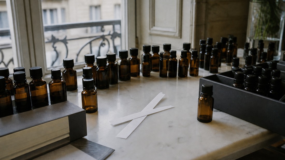 Two scent blotters crossed on a marble bench between rows of small unlabeled essence bottles in a Paris workshop