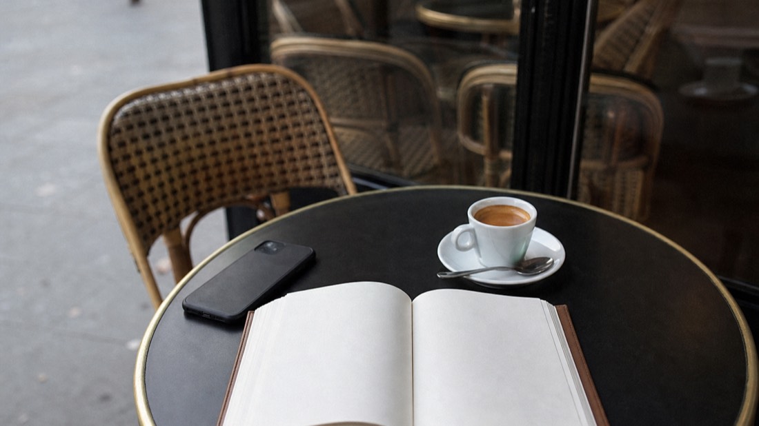 Paper planner open on a cafe table beside a phone and an espresso cup, planning a Paris workshop date