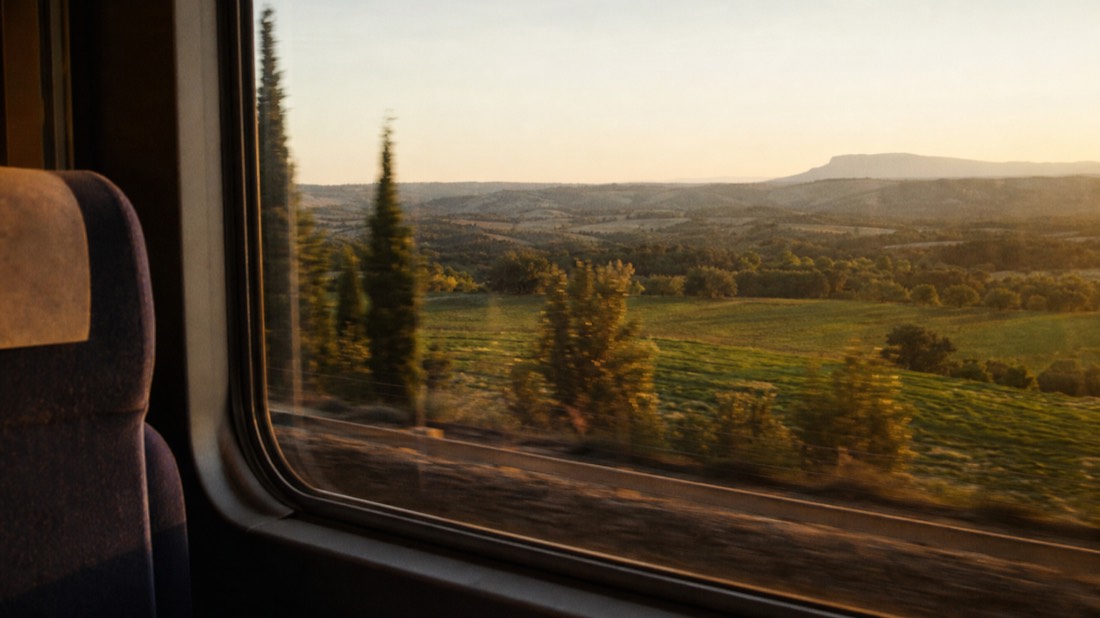 Train window view of Provencal countryside at golden hour with hills and cypress trees blurring past