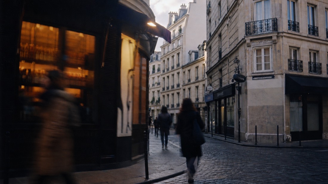 Blurred pedestrians passing a quiet Paris side street corner in changing afternoon light